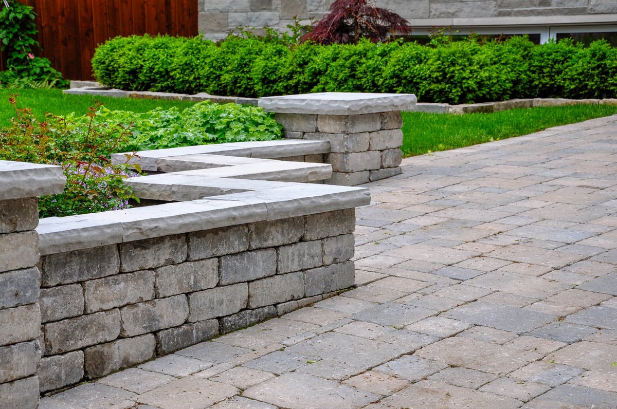 Detail of a retaining wall with pillars and natural stone coping that defines a tumbled paver driveway