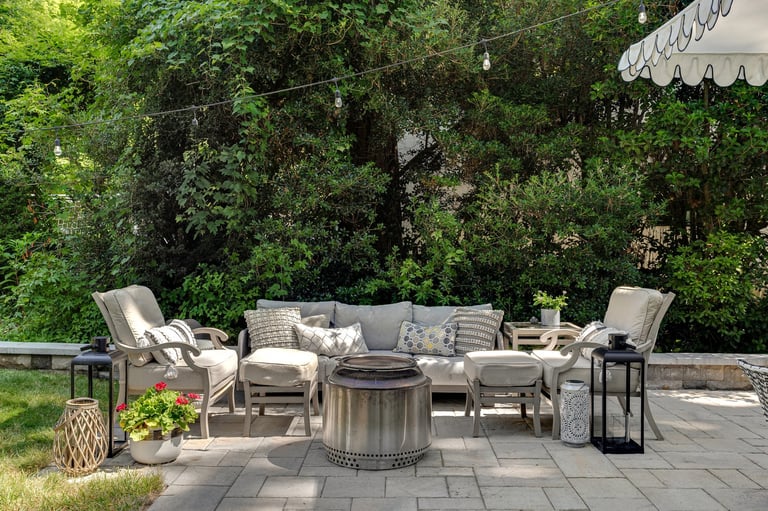 A cozy outdoor seating arrangement featuring cushioned chairs, a fire pit, and lush greenery